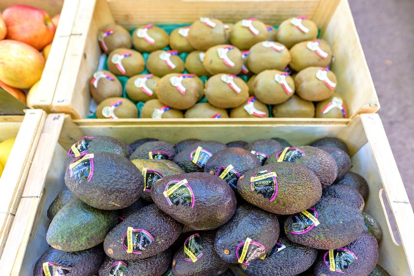 BEAULIEU-SUR-MER, FRANCE - JUNE 28, 2017: Avocado sublime gold, apples and kiwi with stickers in wood boxes for sale in local marketplace.